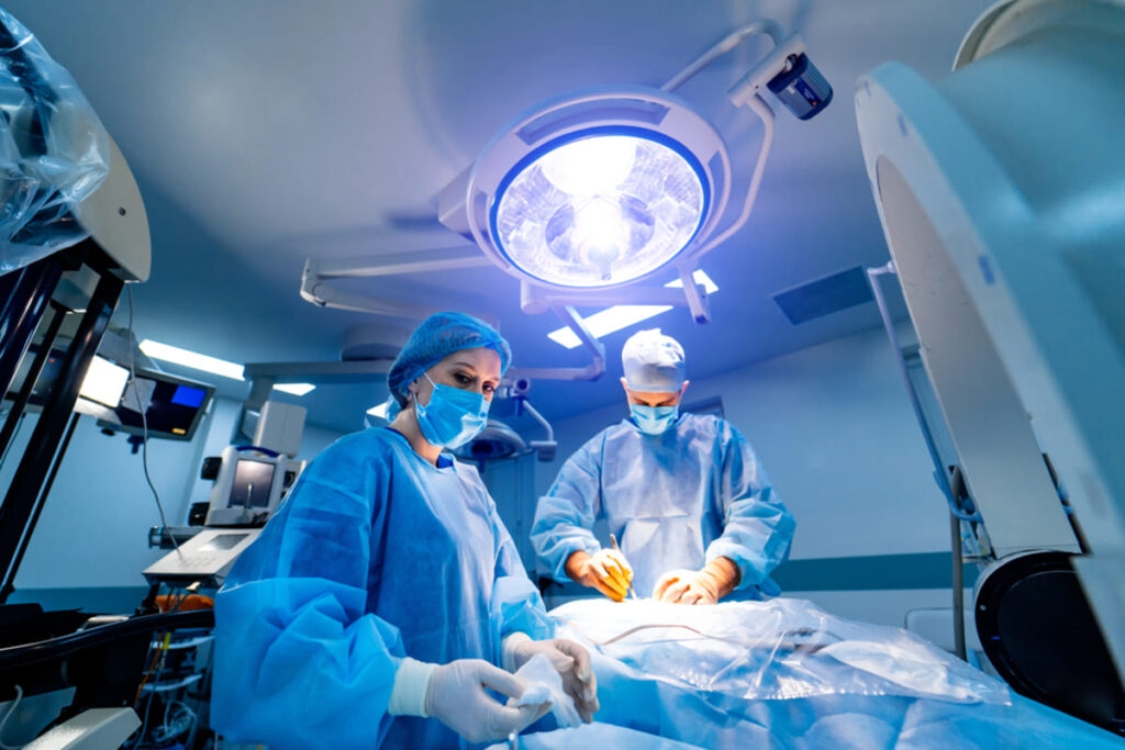 Traumatismele grave, defectele congenitale sau afecțiunile oncologice pot afecta semnificativ calitatea vieții unor persoane. Din fericire, însă, avansul tehnologic din ultimii ani a adus soluții precise și sigure, cum ar fi microchirurgia reconstructivă și microchirurgia pentru replantare. Acest domeniu permite refacerea funcțiilor pierdute și restaurarea aspectului zonei afectate, iar astfel are un impact pozitiv asupra vieții pacienților [1][2]. Află ce presupune o astfel de intervenție, cui îi este adresată, care sunt pașii de urmat, dar și ce avantaje și limite poți întâlni, în cele ce urmează! Ce reprezintă microchirurgia și cum poate ajuta? Chirurgia reconstructivă la nivel microscopic presupune utilizarea unor instrumente extrem de fine, sub ghidajul unui microscop operator. Medicul vizualizează și lucrează cu structuri care, cu ochiul liber, nu pot fi observate corespunzător — de exemplu, vase de sânge cu un diametru foarte mic sau fibre nervoase delicate. Datorită preciziei sporite, echipa reușește să refacă circulația sau să redea sensibilitatea într-o zonă afectată. Astfel, pacienții primesc șansa de a se recupera nu doar din punct de vedere estetic, ci și funcțional [1][2]. La Estetis Clinic, specialiștii abordează cazuri ce altădată păreau fără soluții, folosind metode microchirurgicale actuale în reconstrucție și replantare. Cui se adresează microchirurgia în reconstrucție și replantare? Microchirurgia se dovedește utilă într-o gamă largă de situații: pacienți care au suferit arsuri sau traumatisme ce au distrus țesuturile și care necesită refacerea structurilor și a funcțiilor; femei diagnosticate cu cancer mamar, care au nevoie de reconstrucție post-mastectomie; persoane cu defecte congenitale, precum malformații la nivelul membrelor sau feței; pacienți care au urmat intervenții oncologice extensive sau au avut accidente cu pierdere masivă de țesut. În cazul fiecărui pacient, medicul ține cont de vârstă, afecțiunile asociate și dorința de reintegrare rapidă pentru a oferi soluțiile potrivite [1][3]. Pașii necesari înaintea microchirurgiei: investigații și pregătire Orice pacient potențial eligibil pentru intervenții microchirurgicale parcurge o serie de etape, astfel încât echipa medicală să stabilească cea mai potrivită strategie. Examinarea clinică amănunțită Medicul chirurg analizează leziunea, evaluează starea țesuturilor, circulația locală și posibilitățile de reconstrucție. Investigații imagistice specializate Investigații precum CT (tomografie computerizată), RMN (rezonanță magnetică) sau ecografie Doppler ajută la identificarea vaselor de sânge disponibile și la detalierea afectării structurale. Dacă există suspiciune de afectare neurologică, echipa poate recomanda electromiografie pentru evaluarea nervilor. Analize de laborator adaptate Se realizează analize pentru a exclude infecții sau complicații care pot împiedica o bună vindecare postoperatorie, inclusiv profilul sanguin, inflamator, parametrii coagulării și funcția renală. Evaluare preoperatorie multidisciplinară Medicul anestezist și, când necesar, alți specialiști (diabetolog, cardiolog) stabilesc dacă pacientul poate suporta procedura și care sunt ajustările necesare pentru siguranță maximă. Planificarea detaliată a intervenției Echipa stabilește împreună tehnica optimă (replantare, reconstrucție cu lambou, grefare etc.) și aleg materialele, instrumentarul, dar și modul de abordare chirurgicală pentru recuperare eficientă. Pregătirea meticuloasă reduce rata complicațiilor. La Estetis Clinic, evaluarea include protocoale bazate pe modele internaționale recunoscute [1][2][3]. Ce să faci atunci când te confrunți cu o urgență? Dacă a avut loc un accident care a implicat o amputație, iată ce măsuri trebuie să iei: Recuperează segmentul amputat, înfășoară-l în tifon ușor umezit cu ser fiziologic și pune-l într-o pungă curată, sigilată; Așază punga pe gheață, fără contact direct (nu îngheța segmentul); Notează ora accidentului și mergi imediat la urgențe (sună înainte dacă poți); Nu spăla energic segmentul, nu aplica antiseptice agresive, nu încerca reatașarea acasă. Cum se desfășoară o intervenție microchirurgicală complexă?